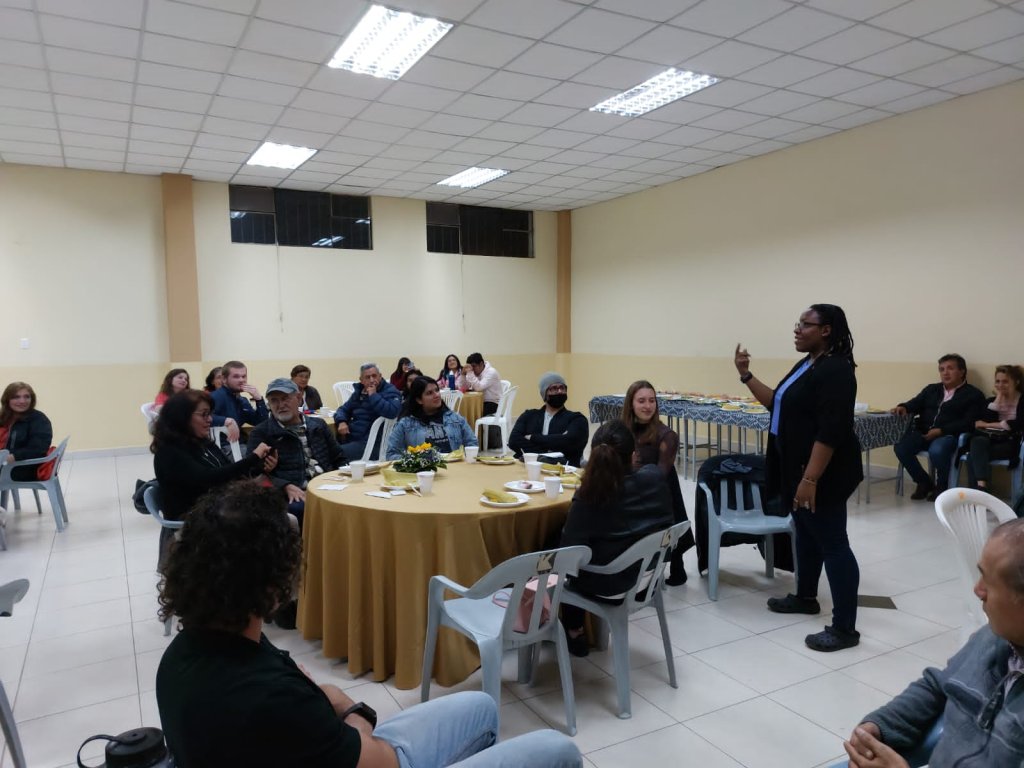 Attendees seated at round tables listening at a gathering.
