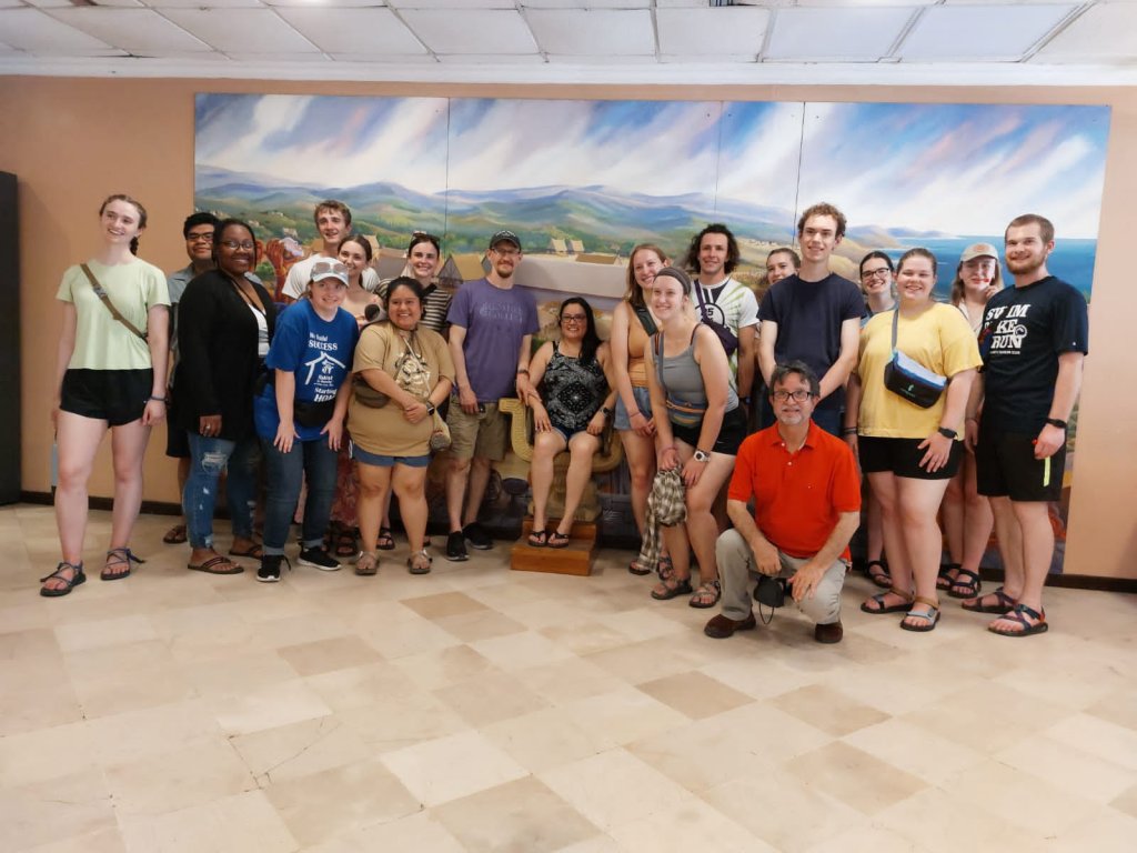 A group photo of students in front of a painted landscape mural.