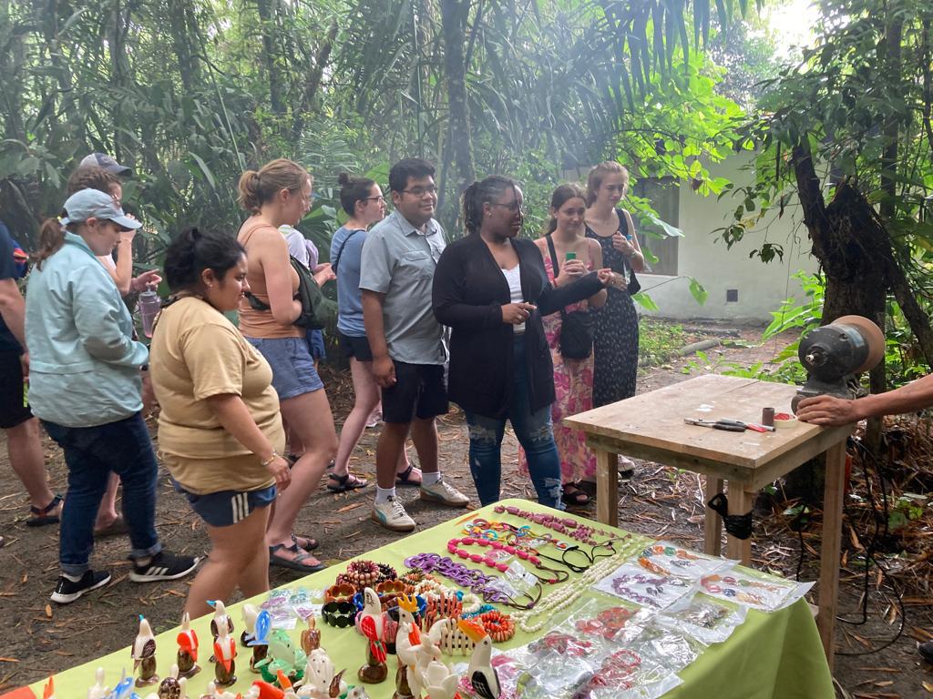 Students looking at a craft vendor's table beneath the trees.