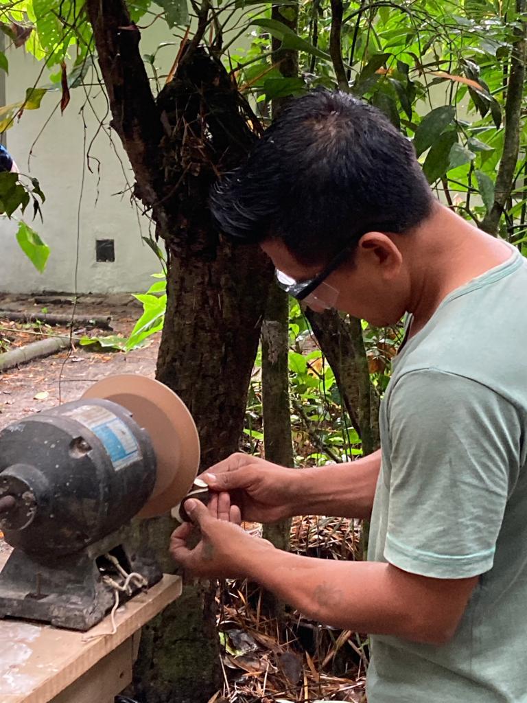 A man working at a grinding wheel among the trees.