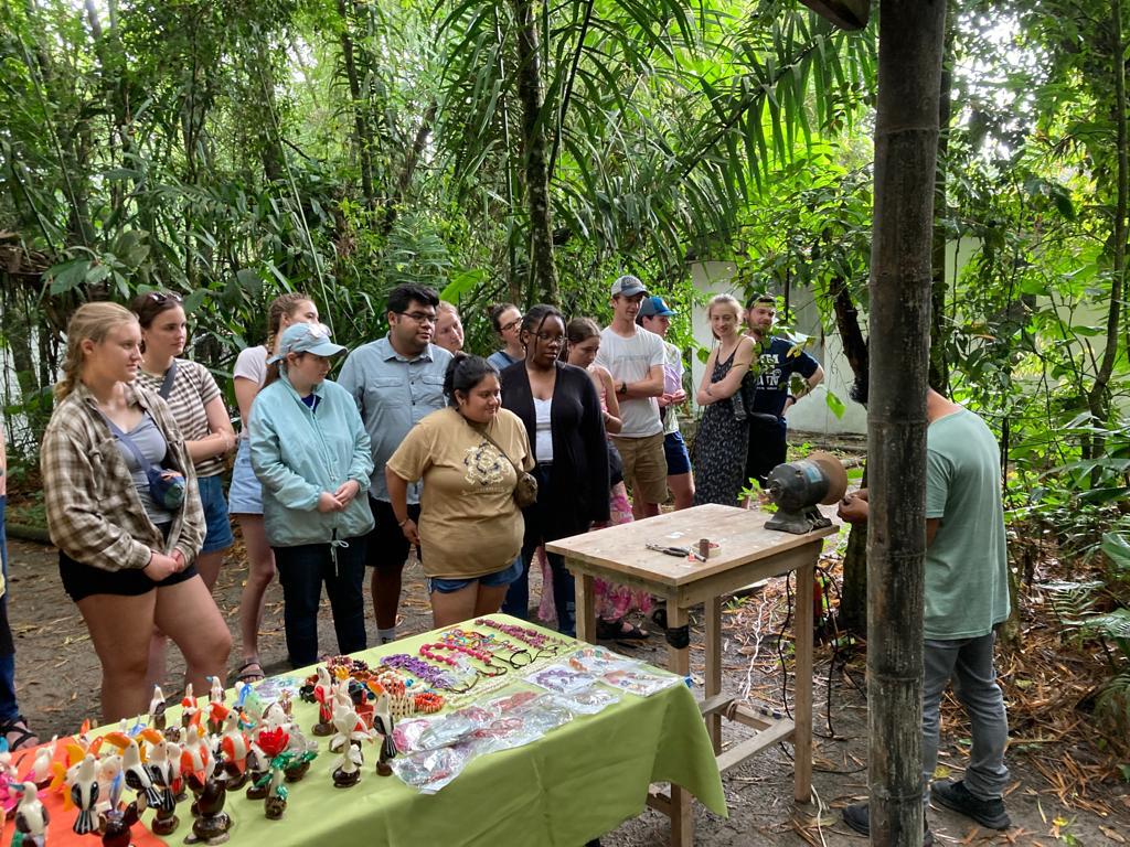 A guide showing crafts to a group beside a display table in the forest.
