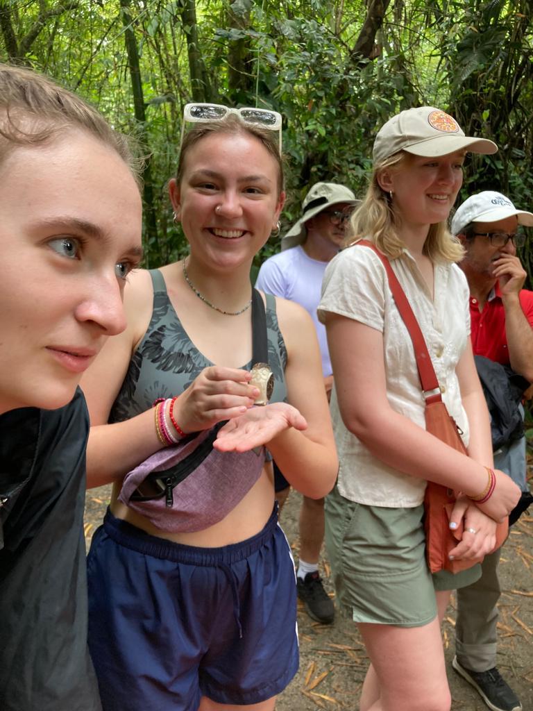 Three young women standing together on a forest trail.