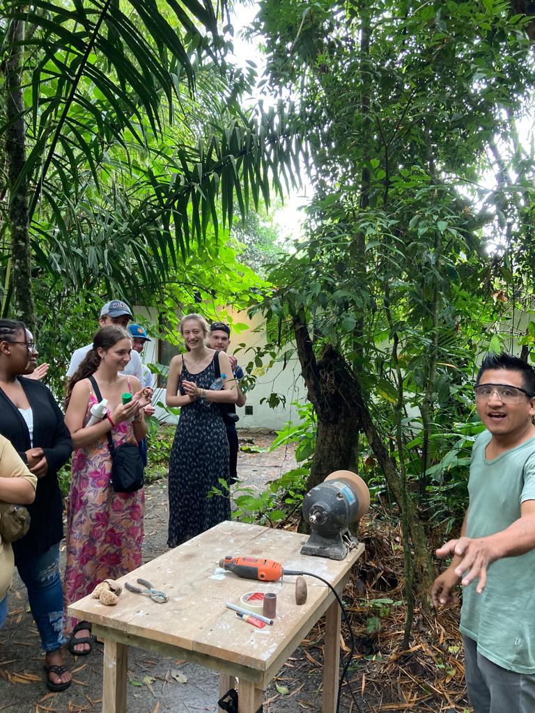 Students watching a craft demonstration among the trees.
