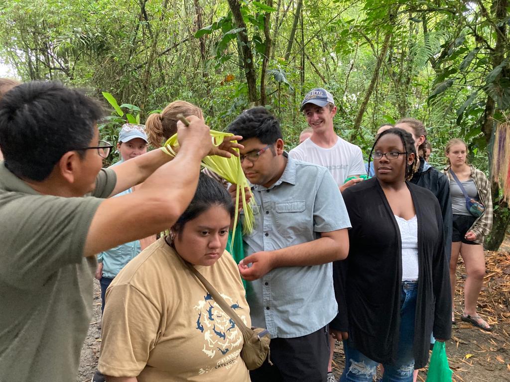 A guide placing a woven straw hat on a student's head.
