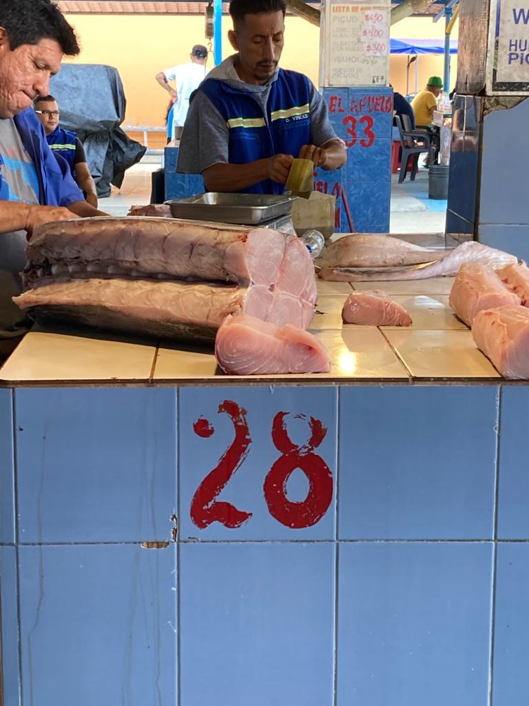 Vendors preparing fish at a market counter marked with the number 28.