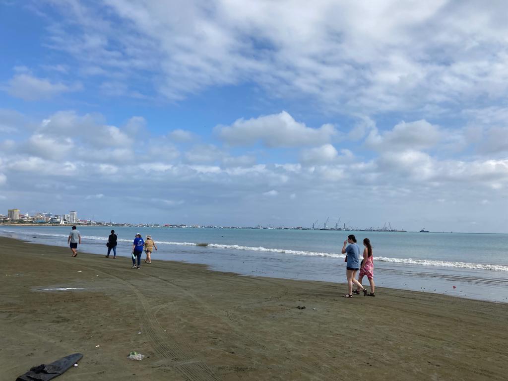 People walking along a wide beach under a cloudy sky.