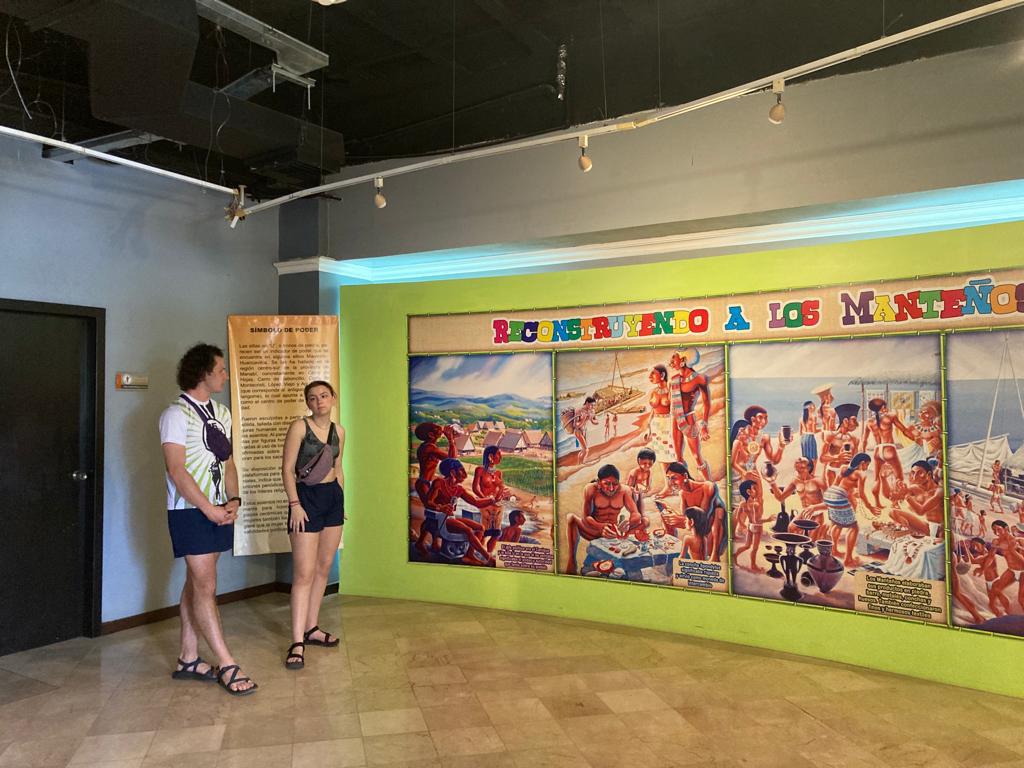Two students standing beside a colorful mural in a museum.