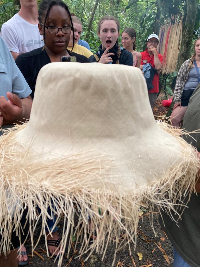 An unfinished straw hat with long fringe on a wooden mold.
