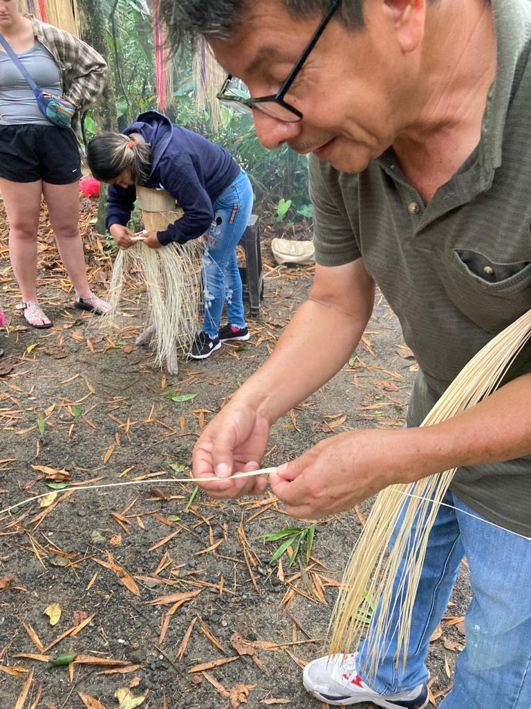 A man demonstrating fiber weaving to students on a forest path.
