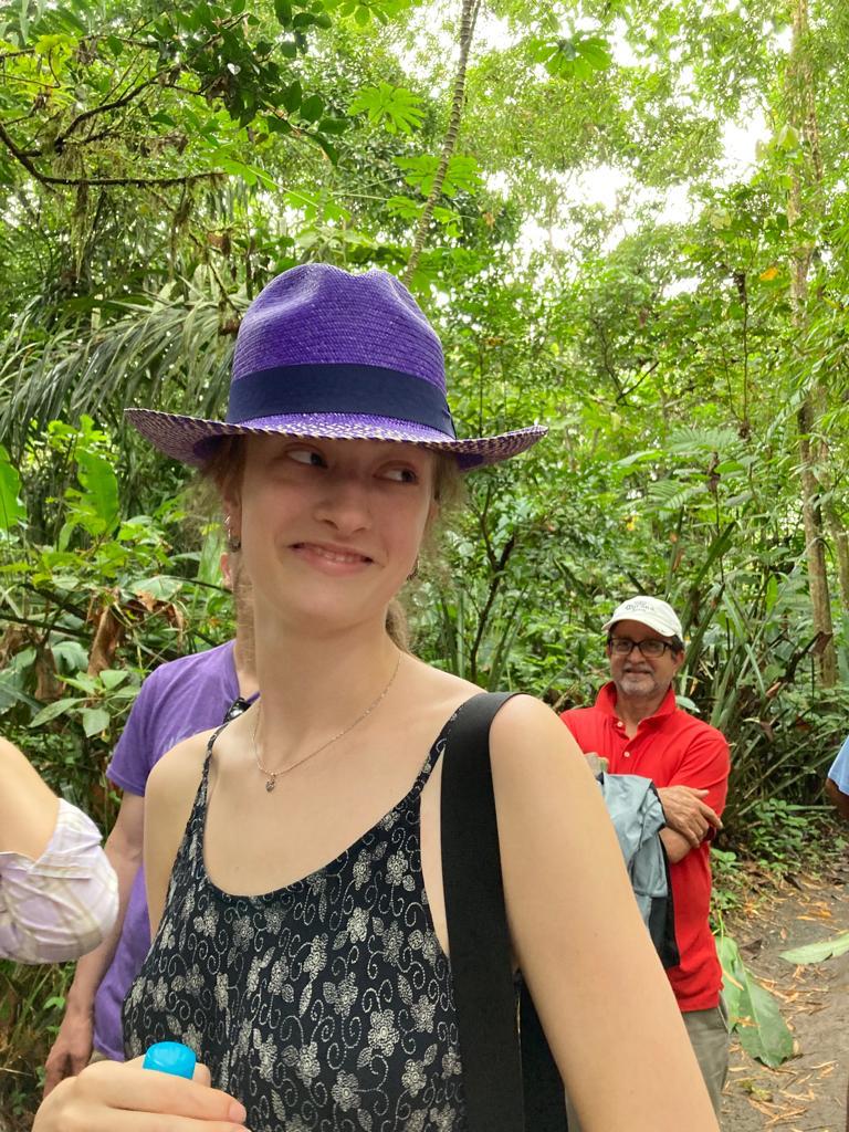 A woman wearing a purple fedora on a jungle path.
