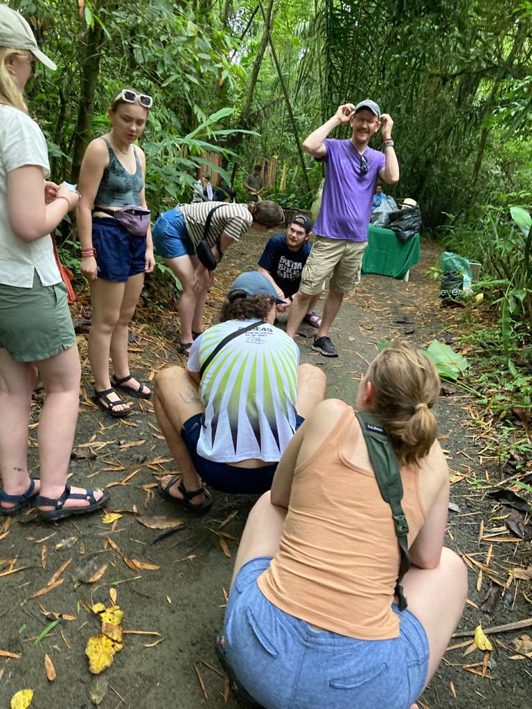 Students crouching to look at something on the forest floor.
