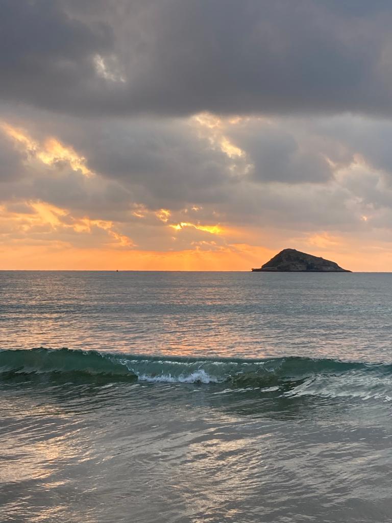 Sunset over the ocean with light reflecting toward a rocky islet.