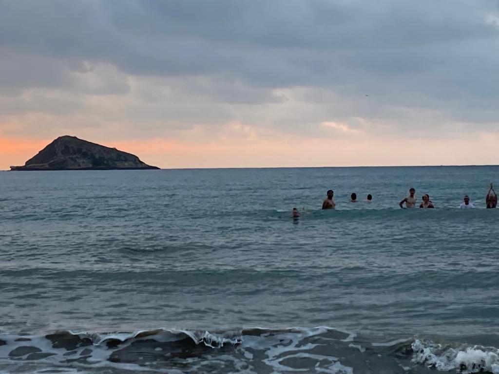 Swimmers in the sea with a rocky islet at sunset.