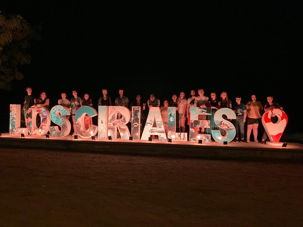 A group standing behind large "LOS FRAILES" letters at night.