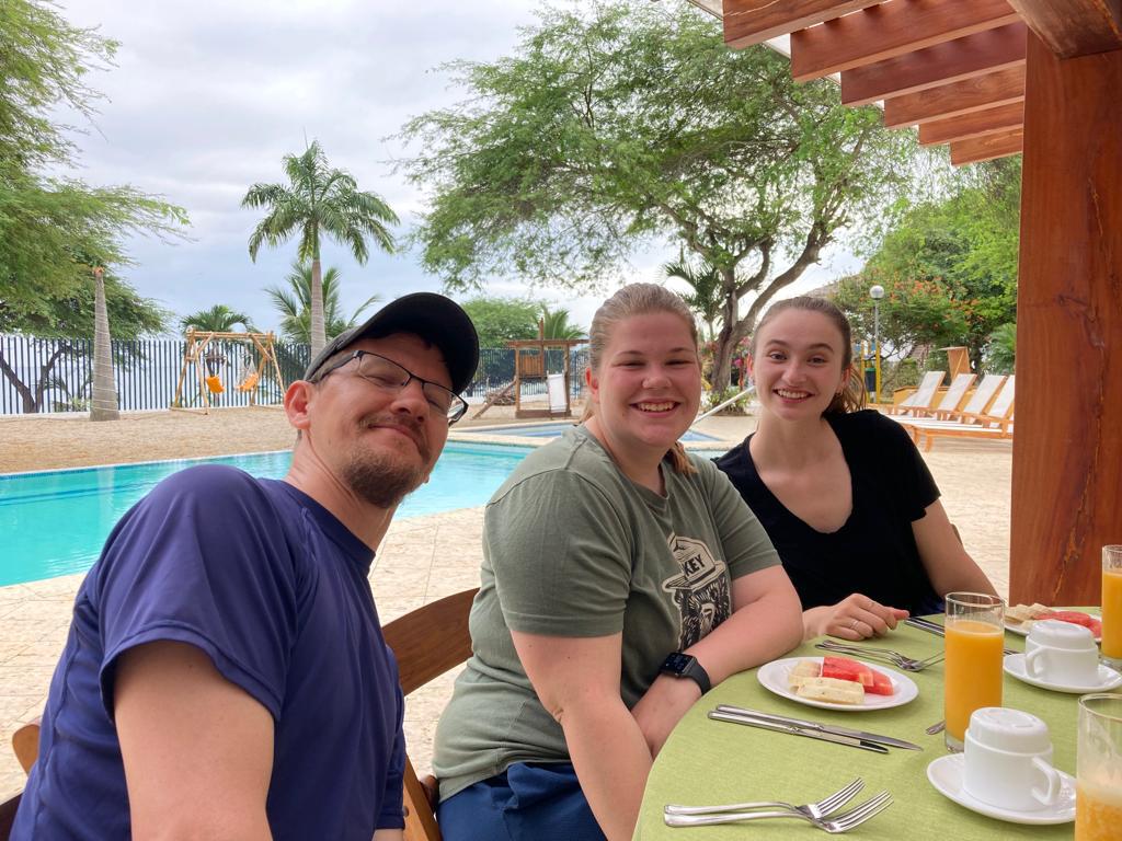 Three people smiling at a poolside breakfast table.