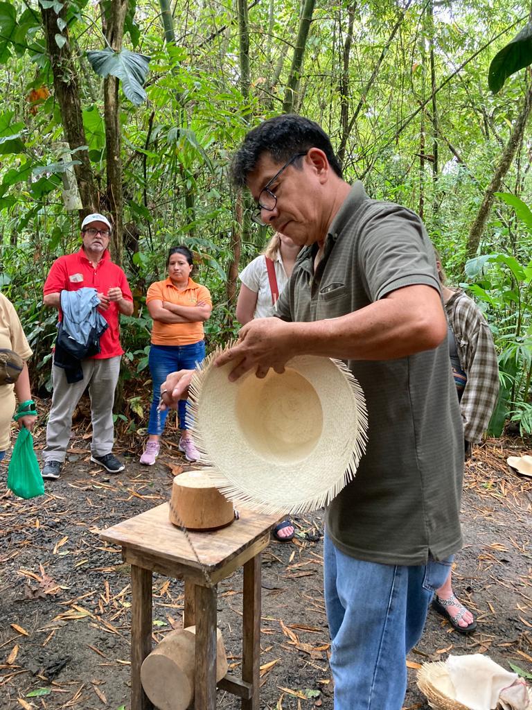 A demonstrator holding up a partly finished straw hat.
