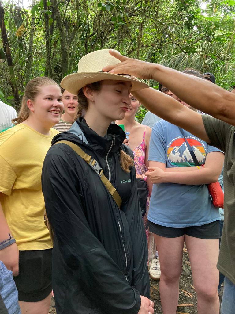 A guide fitting a straw hat onto a student's head.
