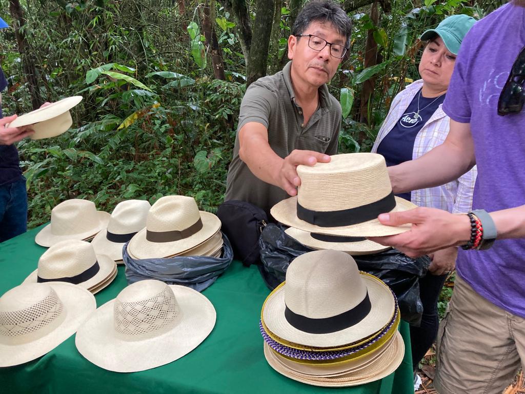 A vendor displaying a table of finished Panama hats to buyers.
