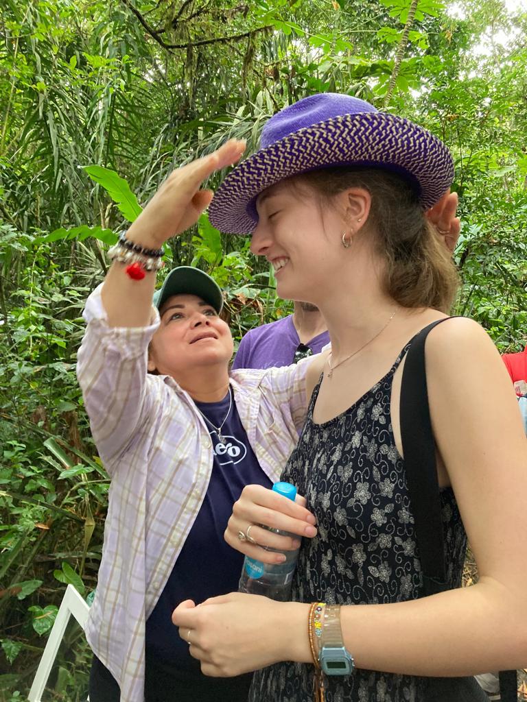 A woman trying on a purple hat with a vendor's help.
