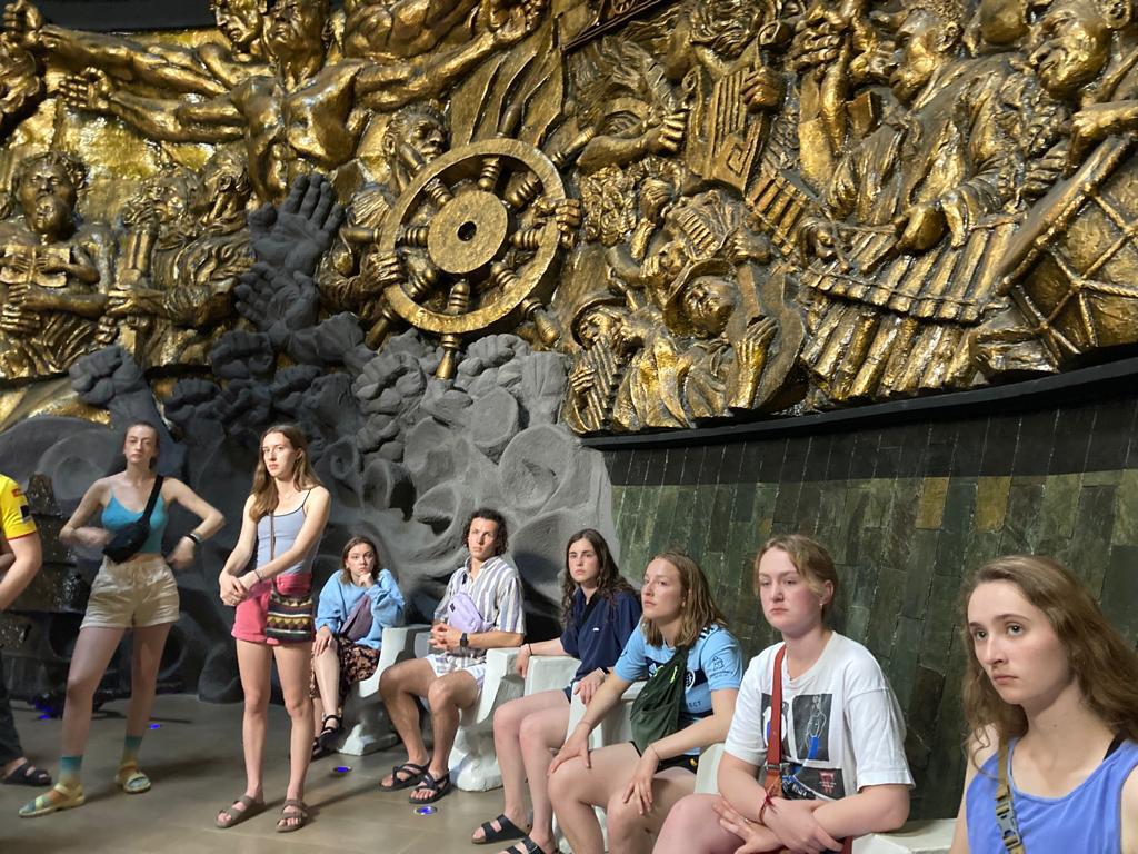 Students posing in a hall filled with elaborate golden sculptures.
