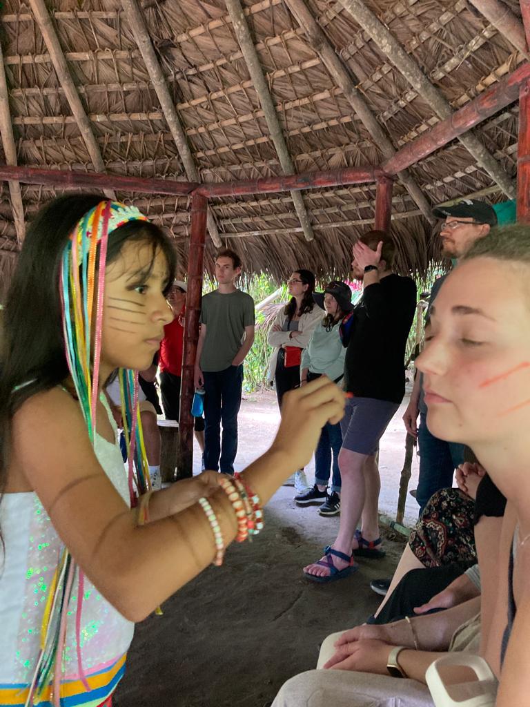 A woman in traditional attire painting a student's face.
