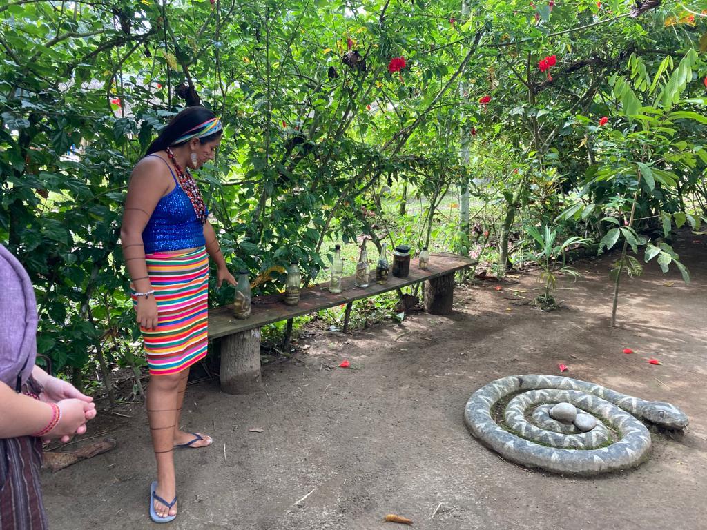 A woman in traditional dress beside a coiled snake figure on the ground.
