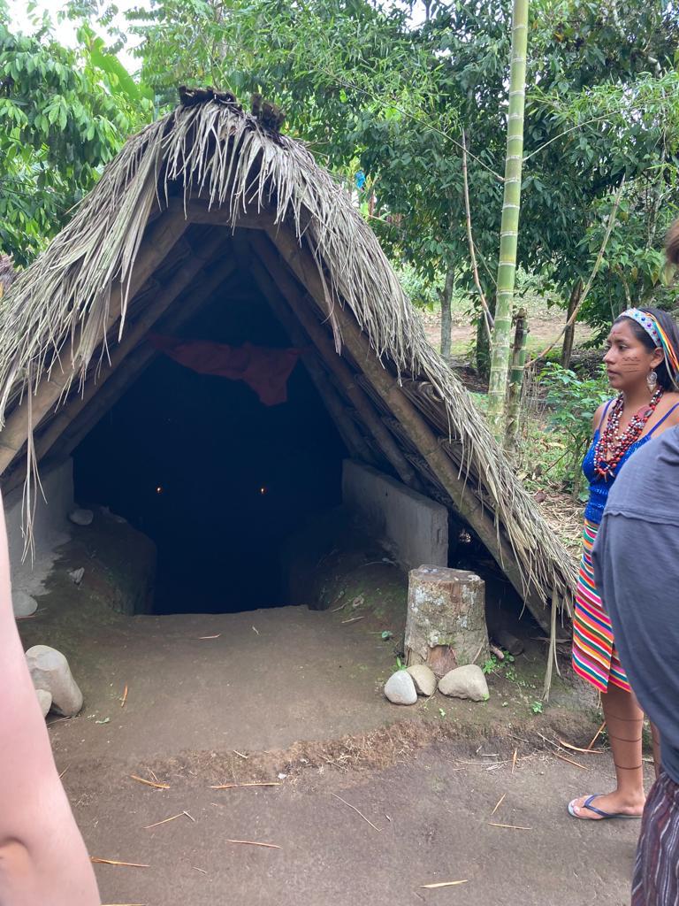 A traditional thatched hut dwelling with people standing outside.
