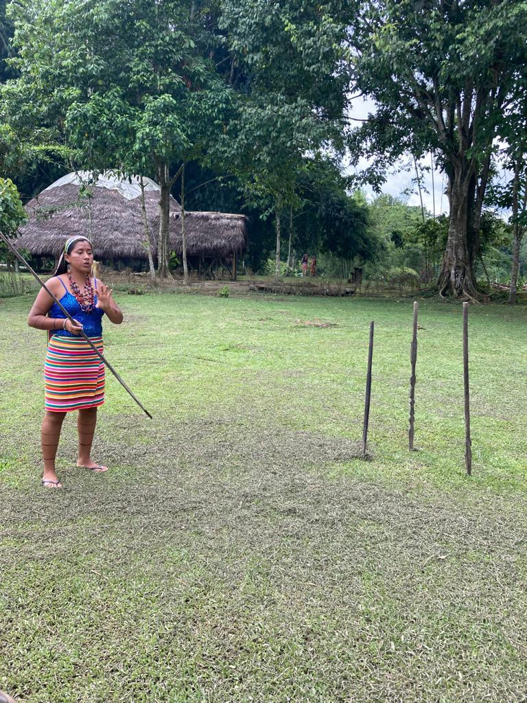 A woman in traditional dress standing on a grassy field with spears.

