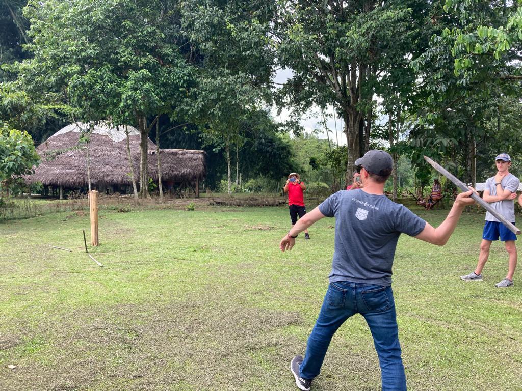 A man demonstrating a spear throw as others watch on the grass.

