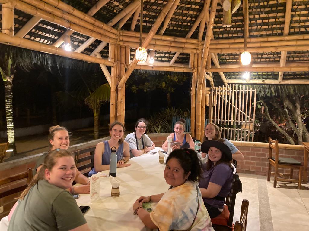 Students seated at a table in a rustic bamboo restaurant at night.
