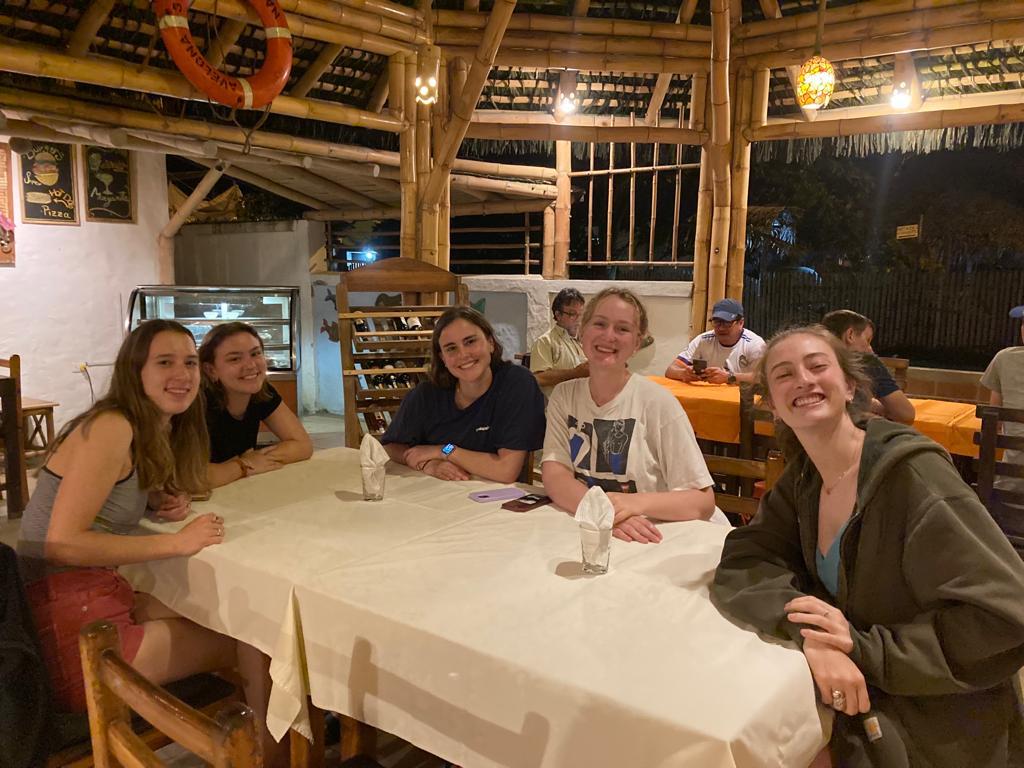 Students smiling around a dinner table in a rustic restaurant.
