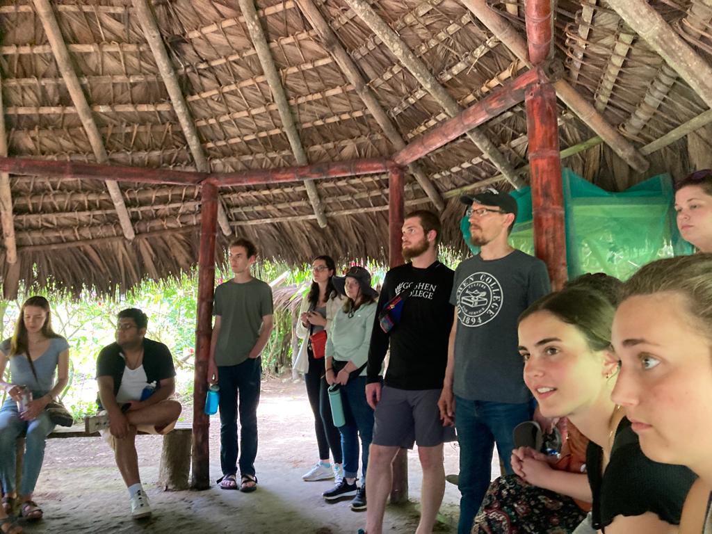 A group of students standing together under a thatched shelter.
