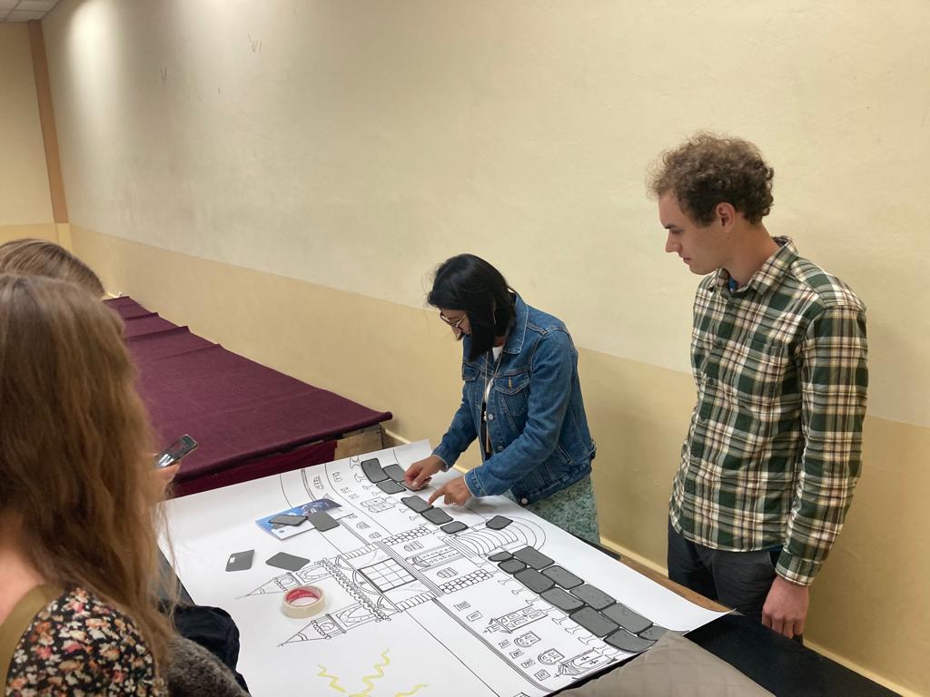 Students looking at printed materials on a table with a woman.
