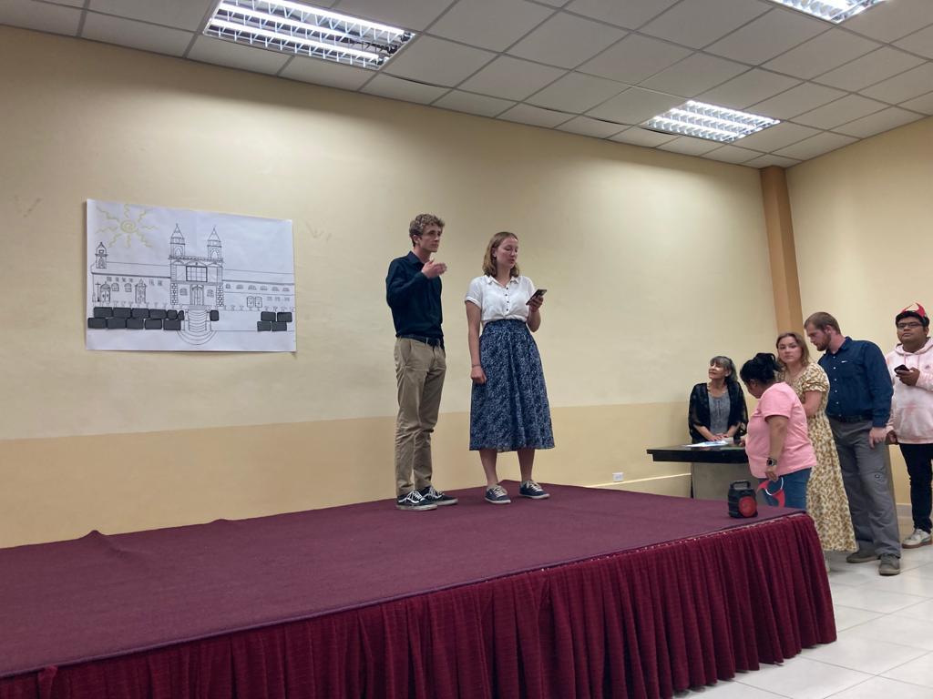 Two students standing on stage beside a printed backdrop.

