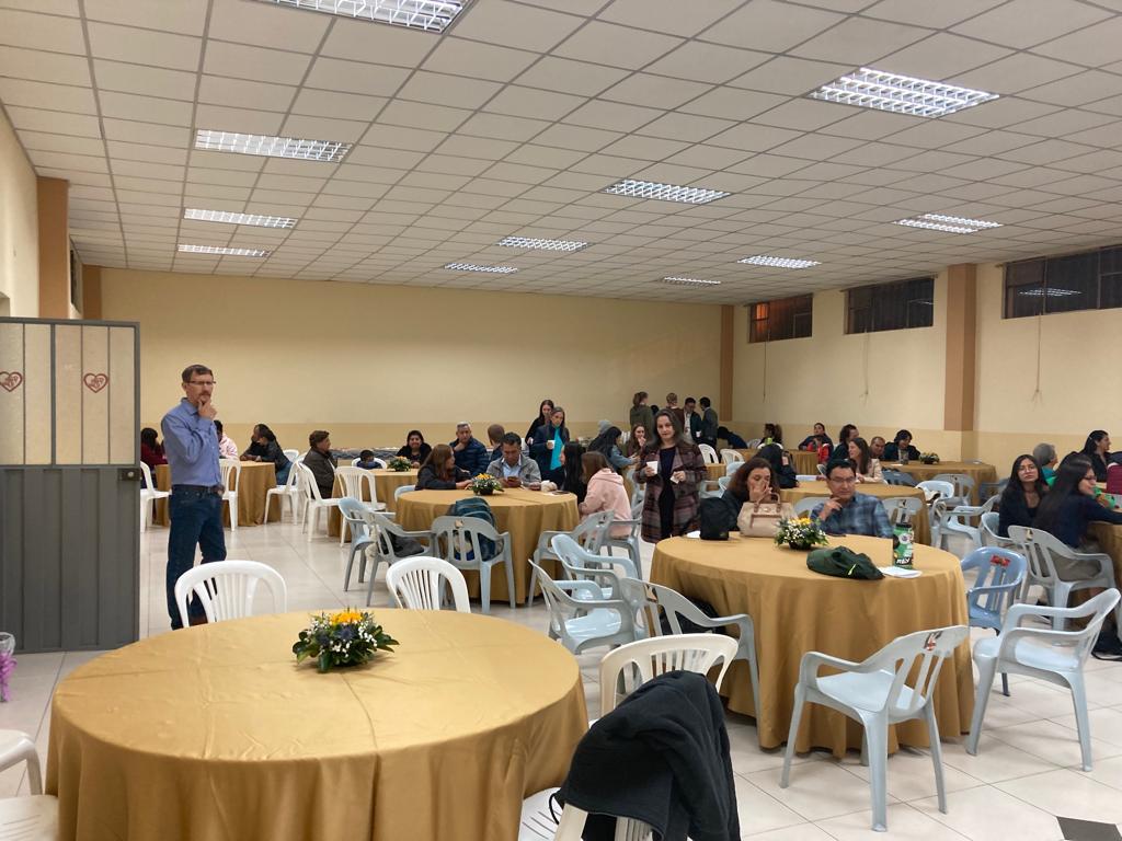 A man speaking to a seated audience in a banquet hall.
