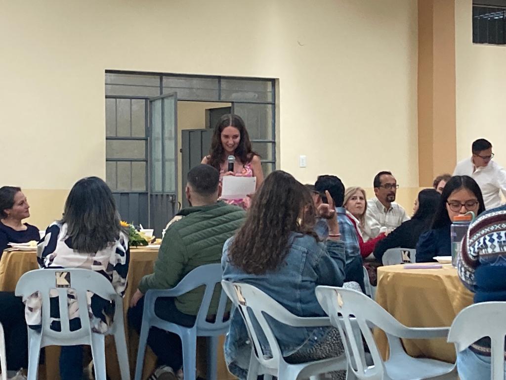 A student speaking to attendees seated at banquet tables.
