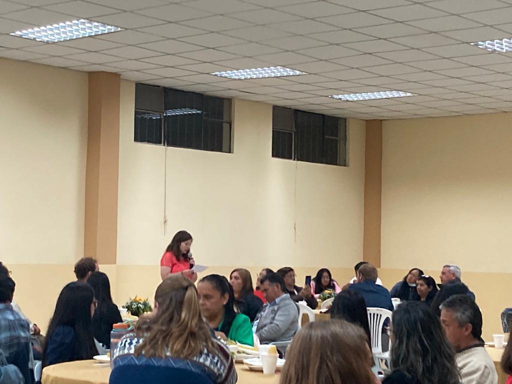 Guests seated at tables during a presentation in a hall.
