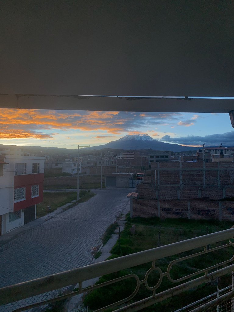 A sunset over a town with a mountain silhouette in the distance.
