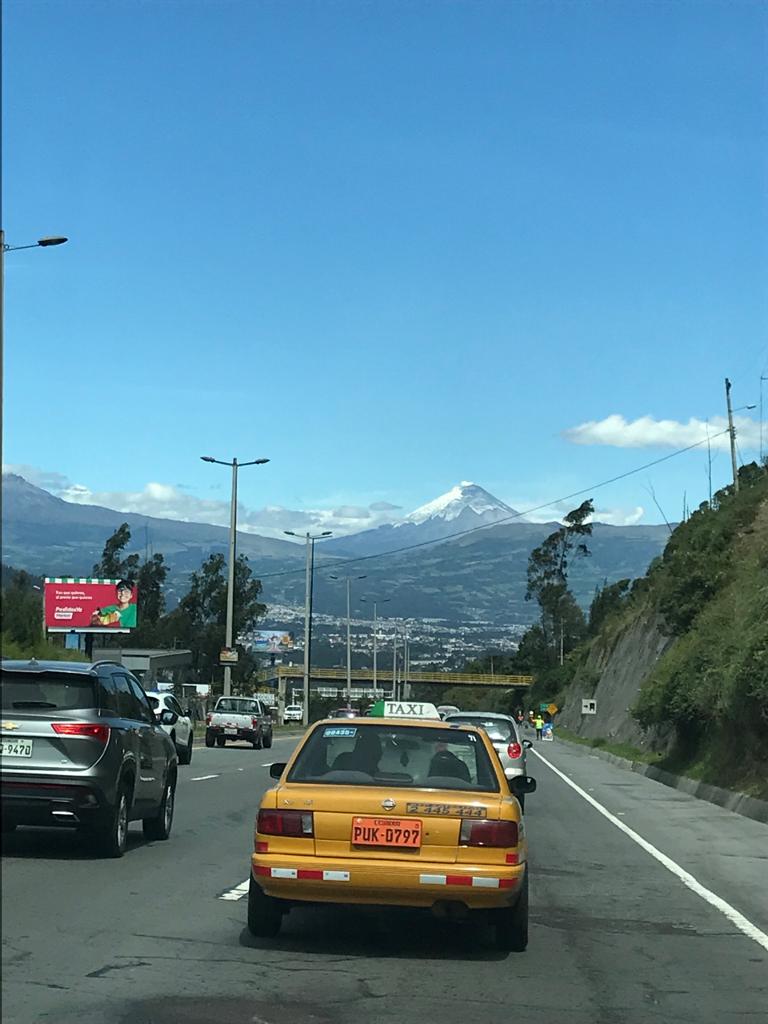 A highway with a yellow taxi and a snow-capped volcano ahead.
