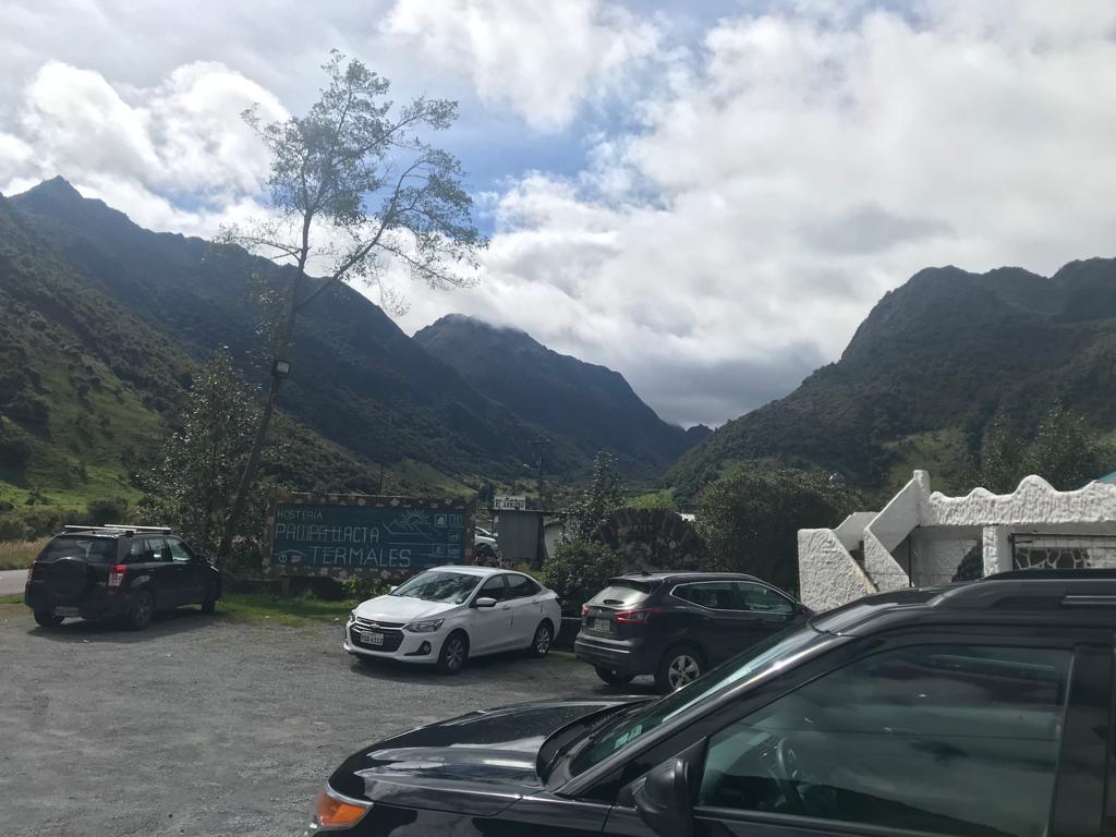 A parking lot at the foot of steep green mountains under clouds.